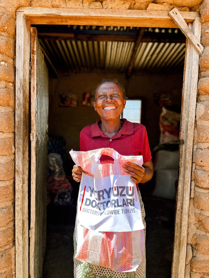 about-us Smiling woman holds donation bag from Doctors Worldwide Turkey in a rustic setting.