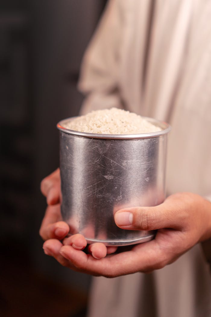 services-01 Close-up of hands holding a tin cup full of uncooked white rice, symbolizing abundance.